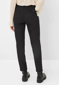 Pantaloni neri su misura con una texture liscia, dotati di due tasche posteriori e dettagli sottili. Abbinati a stivali neri alla caviglia.