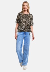 Top s krátkým rukávem s leopardím vzorem v béžové a černé barvě, v kombinaci s světle modrými kalhotami širokého střihu. Outfit obsahuje šňůrkový detail v pase.