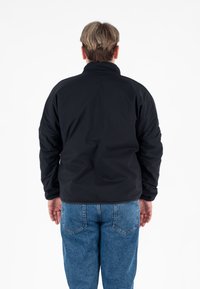 Czarna kurtka softshell z wysokim kołnierzem, z długimi rękawami i gładkim, matowym wykończeniem, noszona na jasnoniebieskich dżinsach.