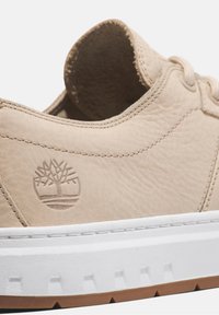 Beige lädersneakers med en strukturerad yta, vit mellansula och brun yttersula. Har diskret logotypdetalj nära hälen.