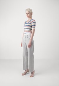 Prugasta, rebrasta pulover v krem, modri, rdeči in zeleni odtenkih, v kombinaciji s svetlo sivo širokimi hlačami in belimi natikači na peto.