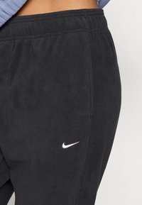 Czarne dresowe spodnie z polaru z białym logo Nike na lewej stronie, z elastycznym pasem i gładką fakturą.