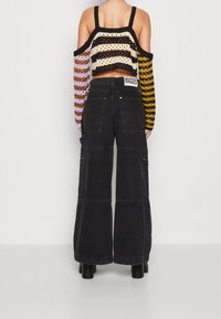 Pantaloni cargo neri a gamba larga con tasche frontali e chiusure zip, abbinati a un crop top in maglia a righe colorate con maniche scoperte.