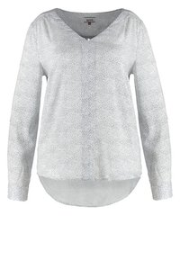 Biała bluzka z długim rękawem o dekolcie w kształcie litery V, z fakturowanym wzorem drobnych czarnych kropek, zaokrąglonym dołem i luźnym krojem.