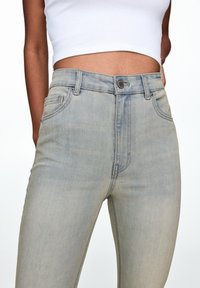 Jeans de mezclilla de cintura alta en un tono azul claro con una textura suave, que cuentan con bolsillos delanteros, cierre estándar de botón y un ligero desgastado.