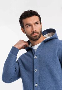 Cárdigan con capucha de textura azul, con un cierre de botones en la parte delantera, que cuenta con un forro interior ligero. Tejido suave y corte relajado.