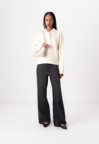 Lounge sweatshirt i krem med polo-krage og brodert detalj, kombinert med vide mørk denim jeans og svarte spisse leppestøvler.