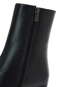 Bottine en cuir noir avec un design élégant, dotée d'une fermeture éclair sur le côté et d'une texture lisse. Le talon est discret et stable.