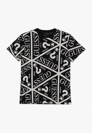 T-shirt noir à manches courtes avec des sections triangulaires blanches portant le mot GUESS, des points d'interrogation et le texte U.S.A., jean, lavé.