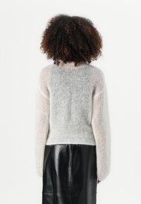 Grå og hvit strikket genser med en avkortet design, med lange ermer og en myk, fluffy tekstur. Kombinert med et svart skinnskjørt.