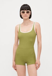Body vert à côtes avec bord blanc, présentant un col en rond et une coupe short. Le modèle porte des lunettes de soleil de couleur claire.