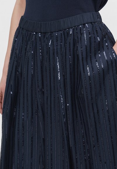 Détail de la taille et de la jupe montrant un tissu noir avec des rayures verticales de sequins brillants, porté avec un haut noir.