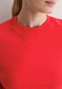 Jasnoczerwona bluza z okrągłym dekoltem wykonana z miękkiego materiału, charakteryzująca się gładką fakturą i subtelnym przeszyciem wzdłuż linii szyi.