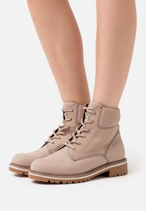 Botas de tobillo beige de cuero con un diseño de cordones, que presentan laterales texturizados, punta redonda y una suela de goma marrón en contraste.