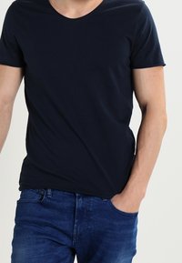 Mörkblå bomullströja med rund halsringning och korta ärmar, tillsammans med blå denimjeans, med avslappnad passform och enkel design.