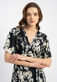 Czarna i kremowa sukienka w kwiaty, z krótkimi rękawami, głębokim dekoltem w serek i miękkim, gładkim materiałem. Posiada zwiewny fason i elegancki wzór.
