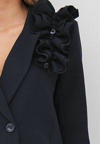 Mornarica blazer s detaljima naborane tkanine na ramenu. Dugmad u odgovarajućoj boji. Glatka tekstura sa strukturiranim oblikom.