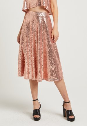 Woman wearing a rose gold sequined midi skirt and matching cropped top, paired with black platform ankle-strap heels.