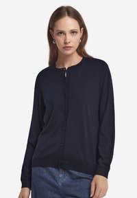 Mörkblå cardigan i mjukt tyg, med rund halsringning, knäppning framtill och långa ärmar. Minimalistisk design utan mönster.