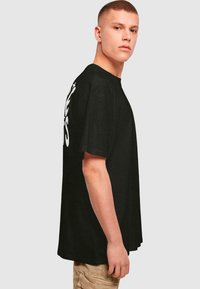 Sort kortærmet t-shirt med løs pasform, prydet med fed hvid tekst på ryggen, lavet af et letvægtsstof.