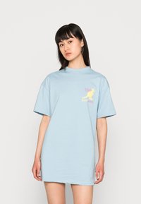 T-shirt oversized de algodão azul claro com mangas curtas e uma estampa gráfica na área esquerda do peito em cores rosa e amarelo.