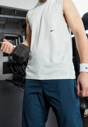 Persoon in een mouwloos wit shirt en blauwe broek tilt een halter van 10 kg op in de sportschool.
