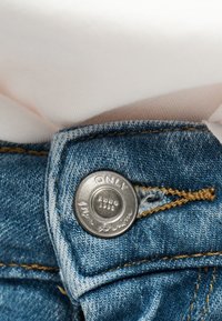 Εγκαρστική λήψη της μέσης ενός μπλε τζιν με μεταλλικό κουμπί με την επιγραφή "ONLY" και λεπτομέρεια πορτοκαλί ραφής στο ύφασμα.