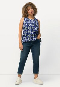 Modrý vzorovaný top bez rukávů s květinovým designem, v kombinaci s tmavými denimovými džíny a bílými teniskami. Top má kulatý výstřih.