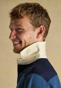 Robustes Kragenhemd mit einem weißen Fischgratmuster am Kragen, navyfarbigen Schulterpaneelen und einem blauen Körper. Glatte Textur und figurbetonter Schnitt.