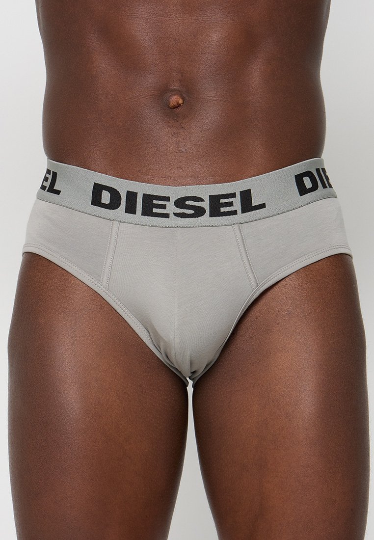 M�ännlicher Oberkörper, der hellgraue Diesel-Unterwäsche mit breitem Bund und schwarzem Diesel-Logo vor einem schlichten Hintergrund trägt.