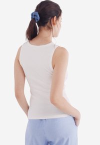 Top a maniche lunghe bianco a coste con scollatura rotonda, caratterizzato da una forma aderente. Abbinato a pantaloni a strisce blu chiaro, completato da un elastico per capelli blu.