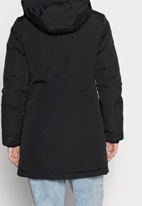 Svart pufferjacka med huva, med en elegant design, slät textur och en insvängd midja för en figurnära silhuett.