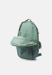 Grön nylonryggsäck med en strömlinjeformad design, som har ett dragkedjade huvudfack och en ytterficka. Mjuk textur med minimala detaljer.