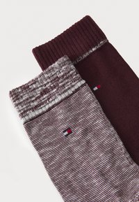 Két pár zokni látható, az egyik egyszínű sötét burgundi, a másik mintás sötét burgundi és szürke keverék, kis logóval.