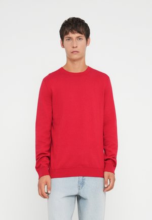 Suéter de punto rojo con cuello de barco y puños acanalados, combinado con jeans de un azul claro. El tejido parece suave y de peso medio.