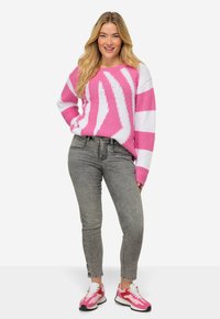 Jersey de punto a rayas rosas y blancas con un corte holgado, combinado con jeans grises y zapatillas rosas con detalles en blanco.