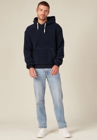 Hoodie en polaire marine avec une poche kangourou, des cordons de serrage blancs et un ourlet côtelé, associé à un jean bleu clair et des baskets blanches.