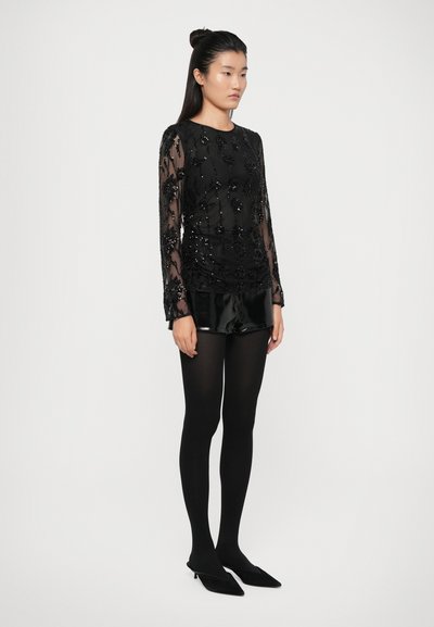 Fekete átlátszó, hosszú ujjú felső virágmotívummal díszítve, fényes fekete sorttal és opál fekete harisnyával párosítva. Lábbeli: fekete, hegyes orrú lapos cipő.