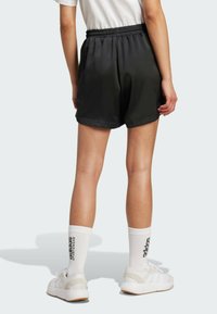 Sorte, satengshorts med elastisk midje, med en avslappet passform og glatt tekstur. Båret med hvite sokker og joggesko.