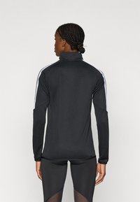 Μαύρο αθλητικό τοπ με μακριά μανίκια και ψηλό γιακά, με λευκές ρίγες στους ώμους. Κατασκευασμένο από απαλό, ελαστικό ύφασμα.