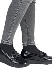 Black patent leather loafers with a round toe, featuring a black chain accent on the front, worn with gray skinny jeans and black socks.