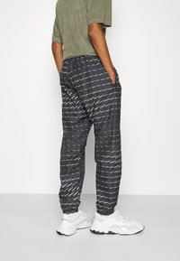 Svarta byxor med ett upprepande mönster av vitt logotyp, elastisk midja, sidofickor och elastiska cirka. Matchat med vita sneakers.