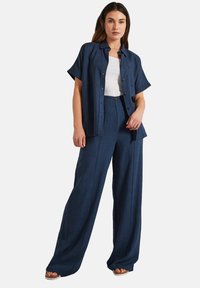 Marinblå linneskjorta med korta ärmar och knäppning framtill, tillsammans med matchande vida byxor. Outfiten har en lös, avslappnad passform.