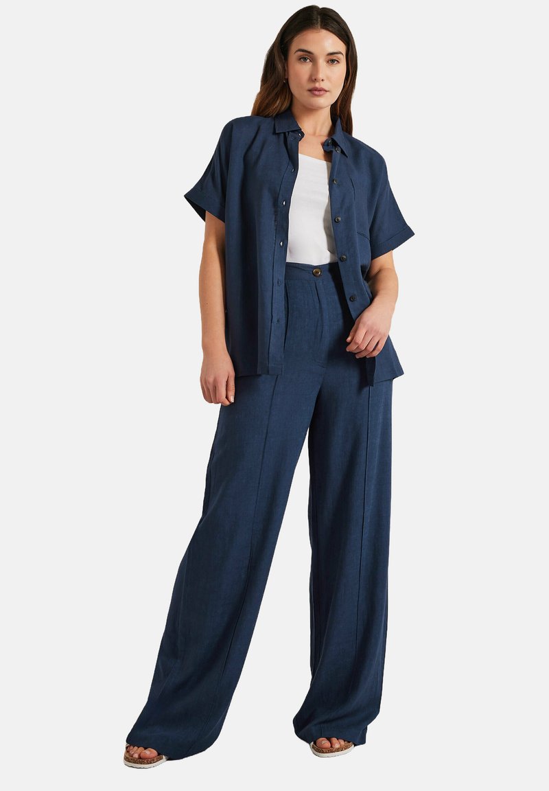 Marinblå linneskjorta med korta ärmar och knäppning framtill, tillsammans med matchande vida byxor. Outfiten har en lös, avslappnad passform.