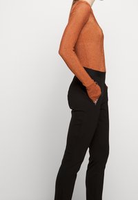 Maglietta a maniche lunghe a coste color ruggine abbinata a pantaloni neri aderenti con tasche laterali e cerniere sottili. Tessuto liscio, design elegante.