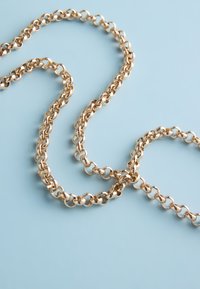 Gold chain with interlocking round links lays loosely coiled on a light blue surface.