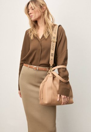 Brązowa bluzka z długim rękawem, beżowa spódnica oraz jasnobeżowa skórzana torebka z regulowanym paskiem, zdobieniami fakturalnymi i zapięciem na sznurek.