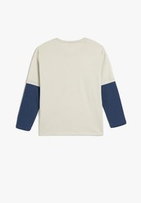 Koszula z długim rękawem w kolorze kremowym z ciemnoniebieskimi rękawami, z okrągłym dekoltem i miękką, gładką fakturą. Prosty design z kolorowym blokowaniem.
