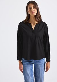 Maglietta nera a maniche lunghe con scollo a V, tessuto morbido e vestibilità leggermente rilassata. Abbinata a jeans azzurri chiari per creare un contrasto.