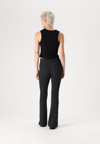 Top sans manches noir associé à un pantalon évasé à rayures noires et blanches, avec une taille ajustée et un tissu texturé.